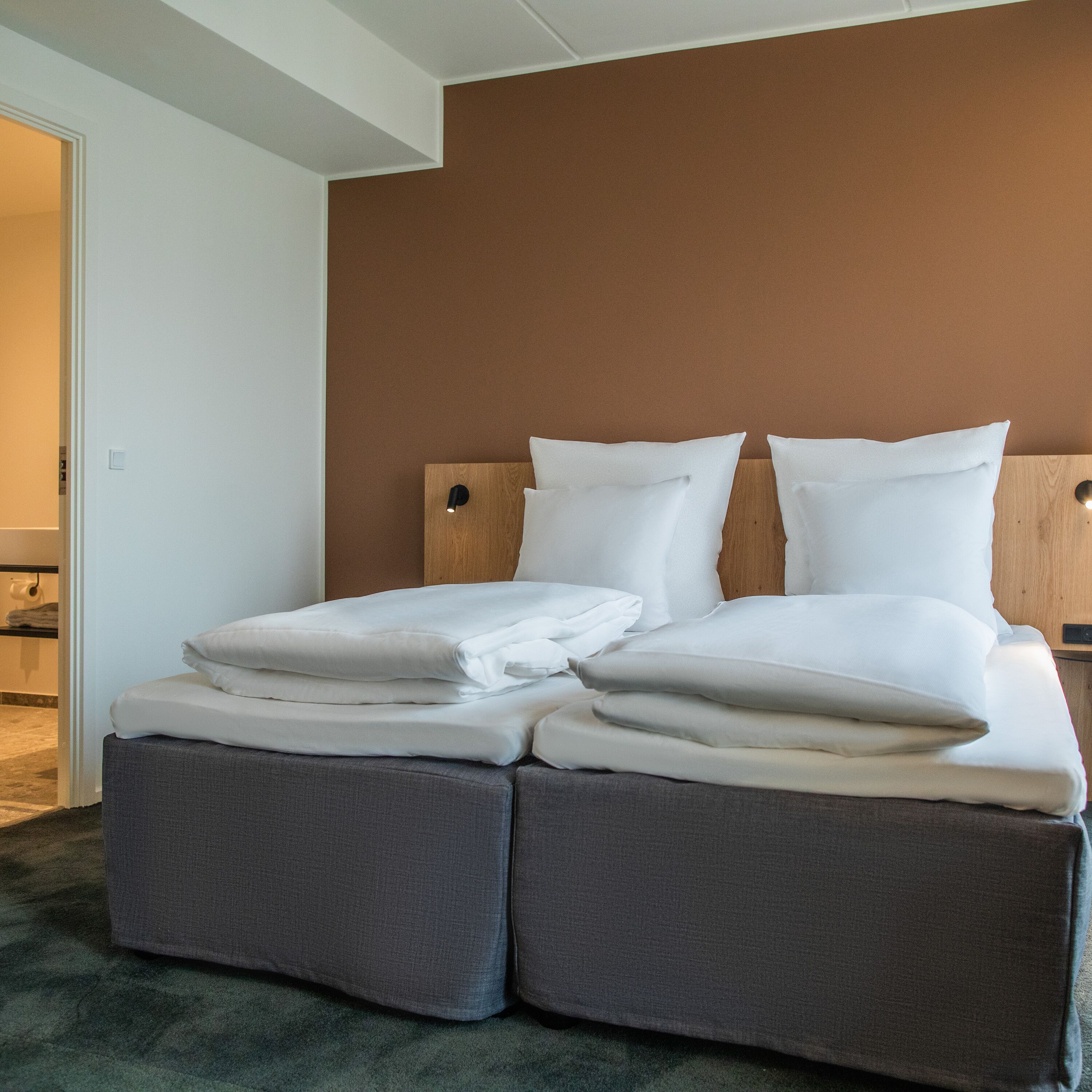 A double bed with a wooden headboard, grey upholstered benches, and a brown wall.