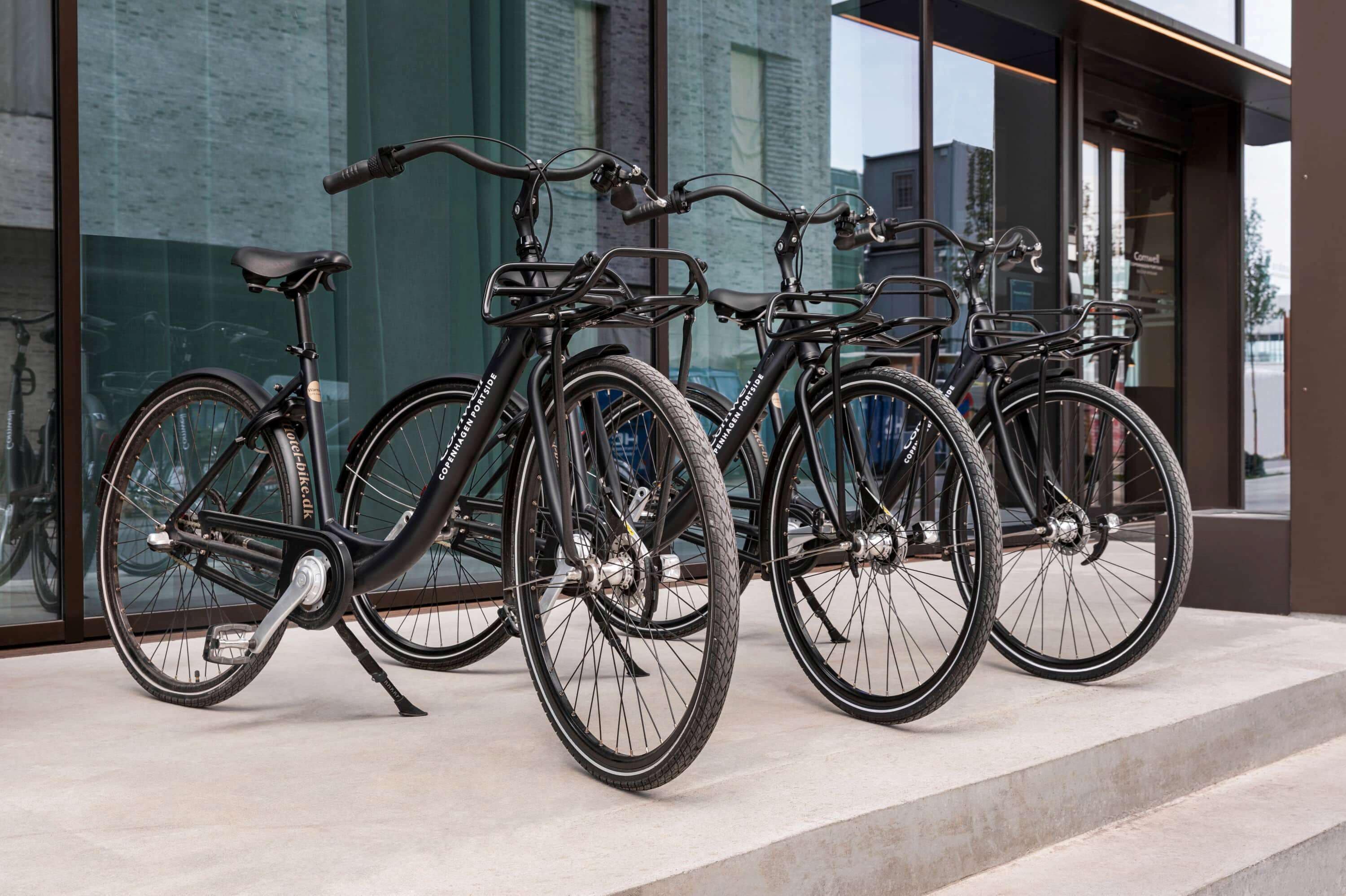 Three bicycles parked in front of a building with large windows.