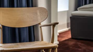 A wooden chair with a curved backrest and armrests, positioned in a room with a dark curtain and a light-colored sofa in the background.