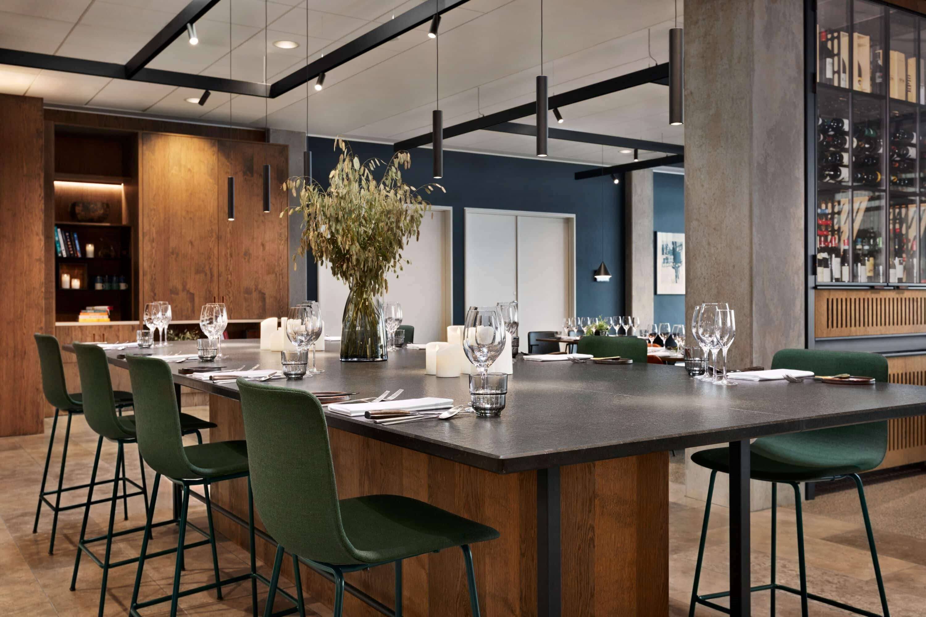 A modern dining area with a long table, green chairs, and a decorative plant centerpiece.