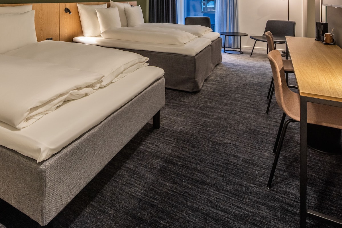 Quarto de hotel com duas camas, uma escrivaninha e uma cadeira.