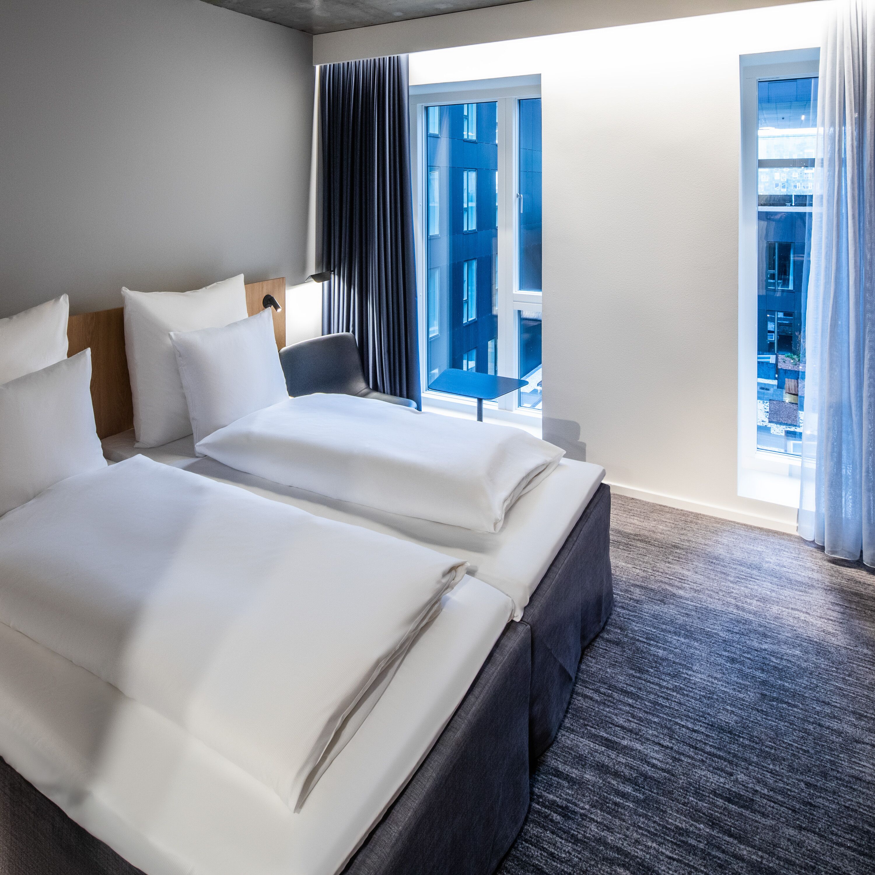Une chambre d’hôtel avec deux lits, une chaise et une fenêtre donnant sur la ville.
