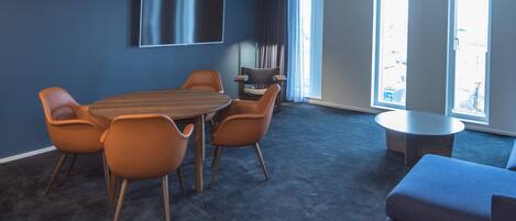 A modern meeting room with a large table, six chairs, a flat-screen TV, and large windows.