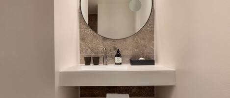 Une salle de bain avec un miroir rond, un lavabo blanc et un porte-serviettes.