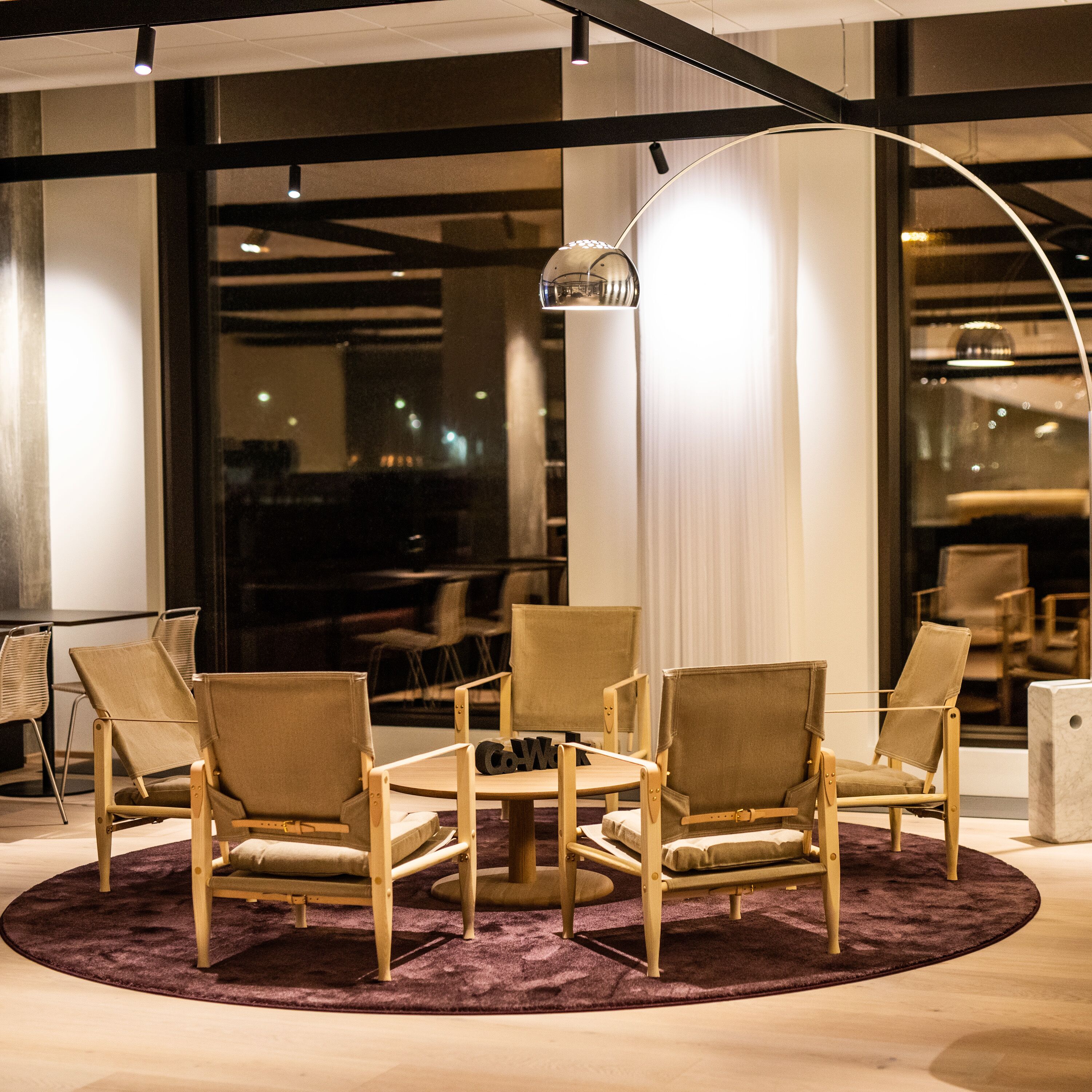 A modern lounge area with a round table surrounded by four chairs, a purple carpet, and a large window with a view of the city.