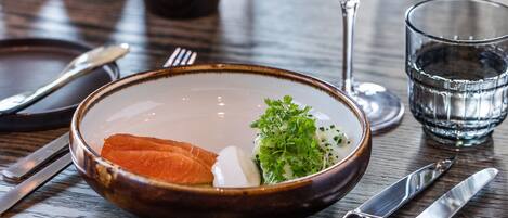 A dining table with a bowl of food, a glass of white wine, and cutlery.