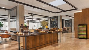 A modern hotel lobby with a central buffet area, seating arrangements, and a bar.