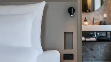 Una habitación de hotel moderna con una cama bien hecha, una lámpara fijada a la pared, un pequeño panel de control y una tarjeta de servicio de ropa.