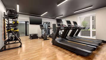 Un gimnasio con cintas de correr, máquinas de pesas y un televisor montado en la pared.