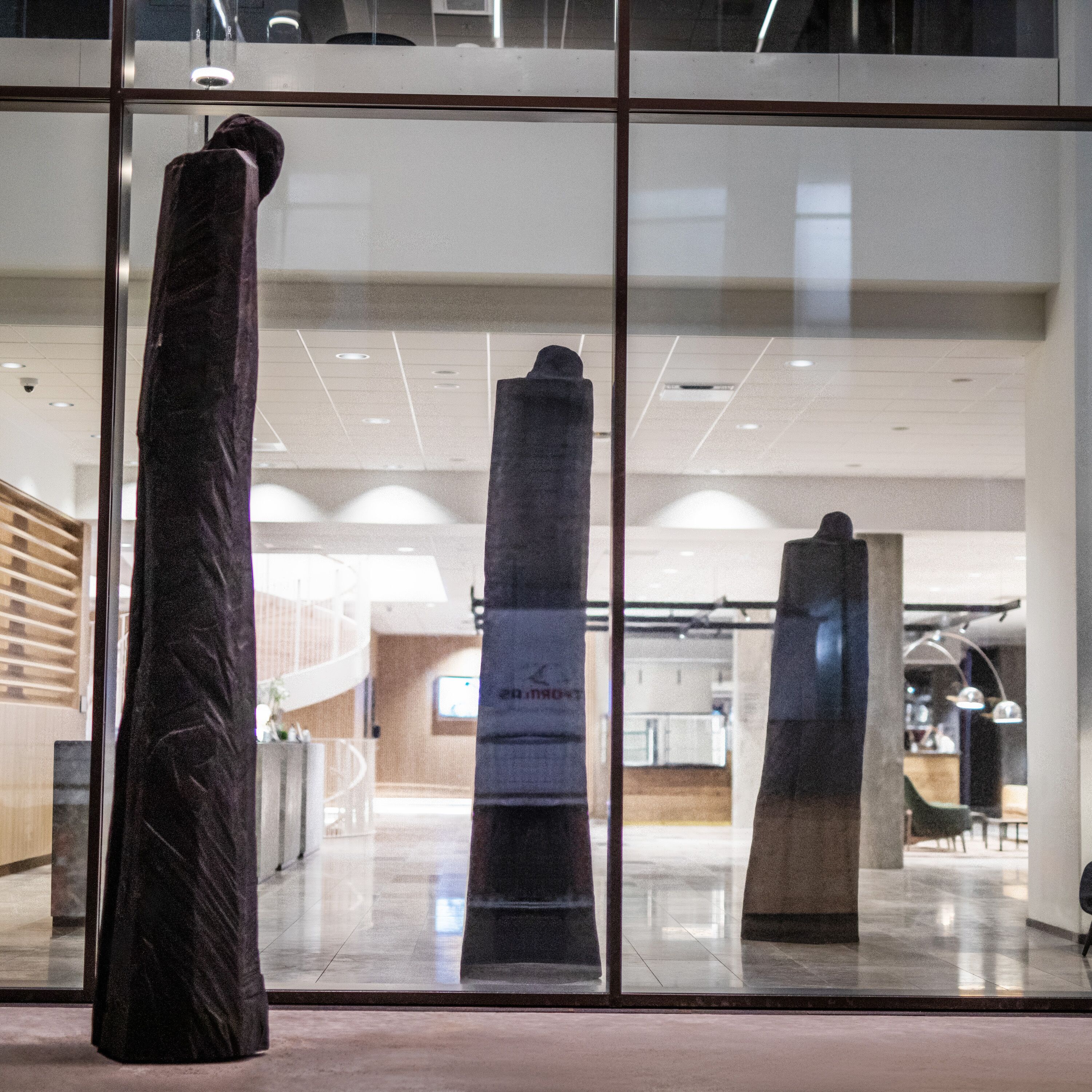 Un interior modern amb grans finestres de vidre, una columna central i una escala que condueix a un nivell superior.