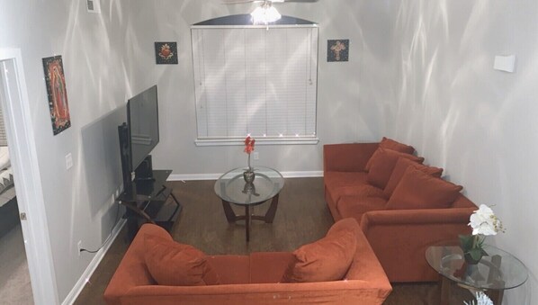 Cozy living space with a sofa set facing a wall-mounted TV, a small table, and framed icons.