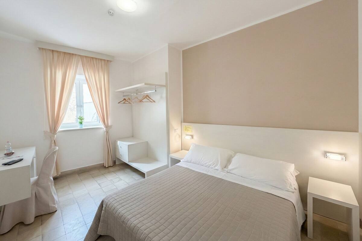 Een minimalistische hotelkamer met een groot bed, nachtkastjes, een bureau en een stoel.