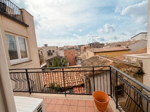A balcony with a terracotta-tiled roof, a potted plant, and a view of neighboring buildings.