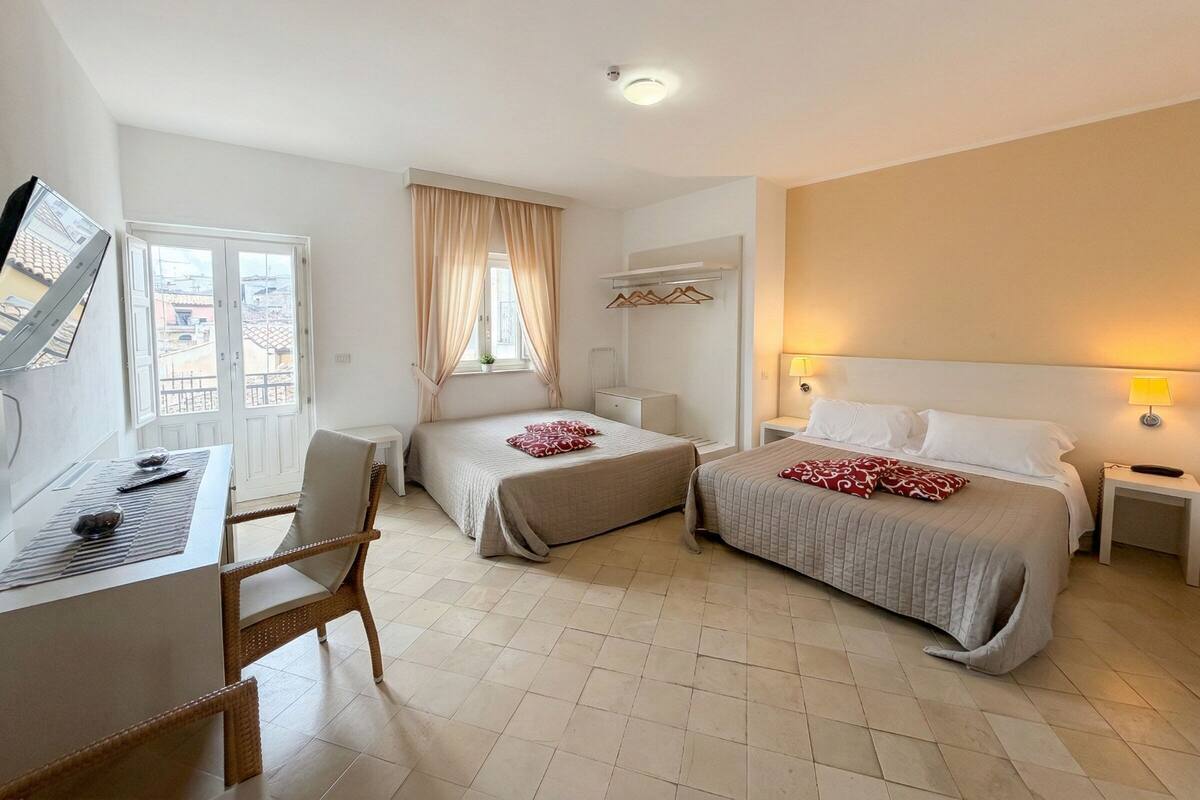 Een hotelkamer met twee bedden, een bureau, een stoel en een raam met gordijnen.