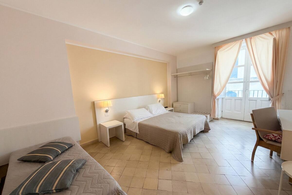 Een hotelkamer met twee bedden, een bank, een stoel, een kleine tafel en een raam met gordijnen.