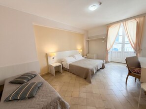 A hotel room with two beds, a sofa, a chair, a small table, and a window with curtains.