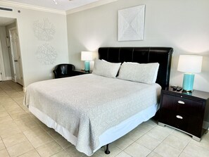 A neatly arranged bedroom with a large bed, two bedside tables with lamps, and a door leading to another room.
