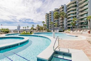 Een hotel met een groot buitenzwembad, meerdere balkons en palmbomen.