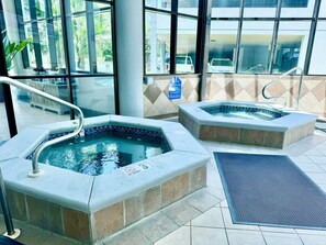 Twee jacuzzi’s met een betegelde vloer en een metalen leuning, een blauw bord en een waterpartij.