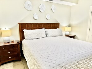 Een opgemaakt bed met een houten hoofdbord, twee nachtkastjes met lampen en decoratieve wandkunst.