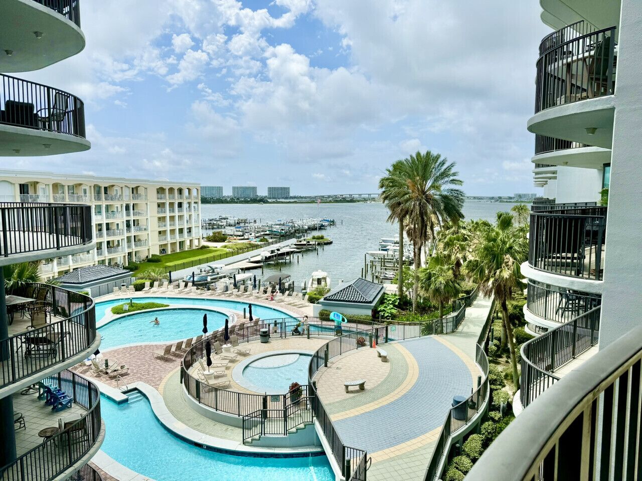 A hotel with a large, circular pool surrounded by a deck, with a marina and boats in the background.