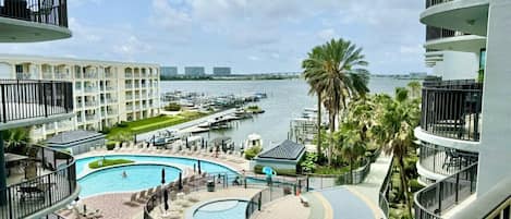 A hotel with a large, circular pool surrounded by a deck, with a marina and boats in the background.