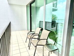 A balcony with four chairs, a glass door, and a view of a building with a balcony.