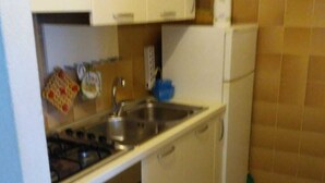 Een kleine keuken met witte kastjes, een gasfornuis, een spoelbak en een koelkast.