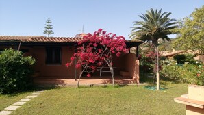 Een huis met een terras, een kleine tuin en een boom met roze bloemen.