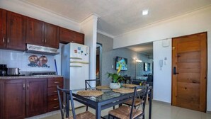 A modern kitchen with wooden cabinets, a refrigerator, and a dining table with chairs. - Cozy 2br-2bt Apt Near The Beach And Main Street (Sosúa)