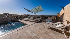 A rooftop pool area with lounge chairs, a large umbrella, and a view of the cityscape. - Palazzo Bifora (Mdina)