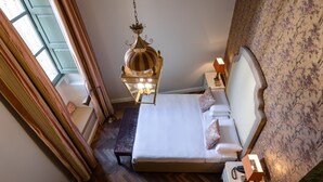 A neatly arranged bedroom with a large bed, a hanging lamp, a bedside table, and a view of the outdoors through a window. - Palazzo Bifora (Mdina)