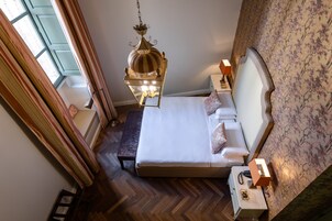 Quarto bem arrumado com uma cama grande, uma luminária pendente, uma mesinha de cabeceira e vista para o exterior através de uma janela.