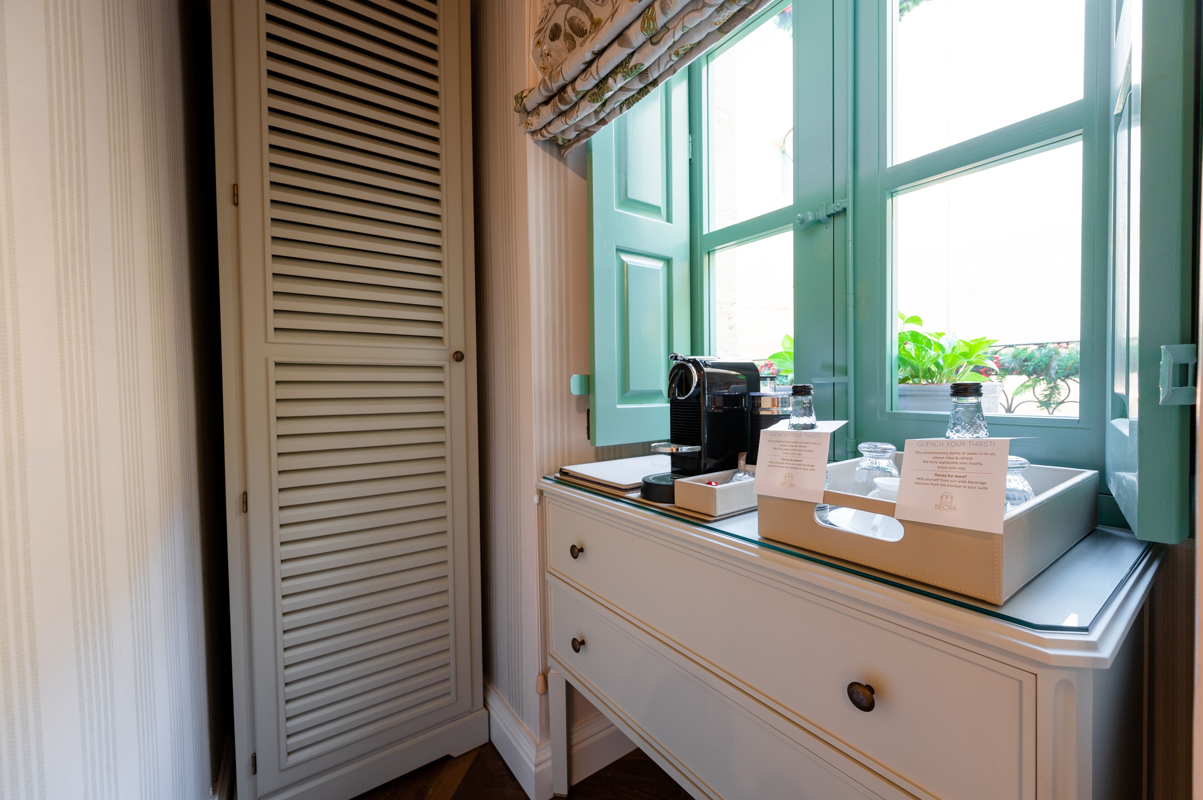 Un baño con tocador blanco, un espejo y una ventana con vistas al follaje exterior.