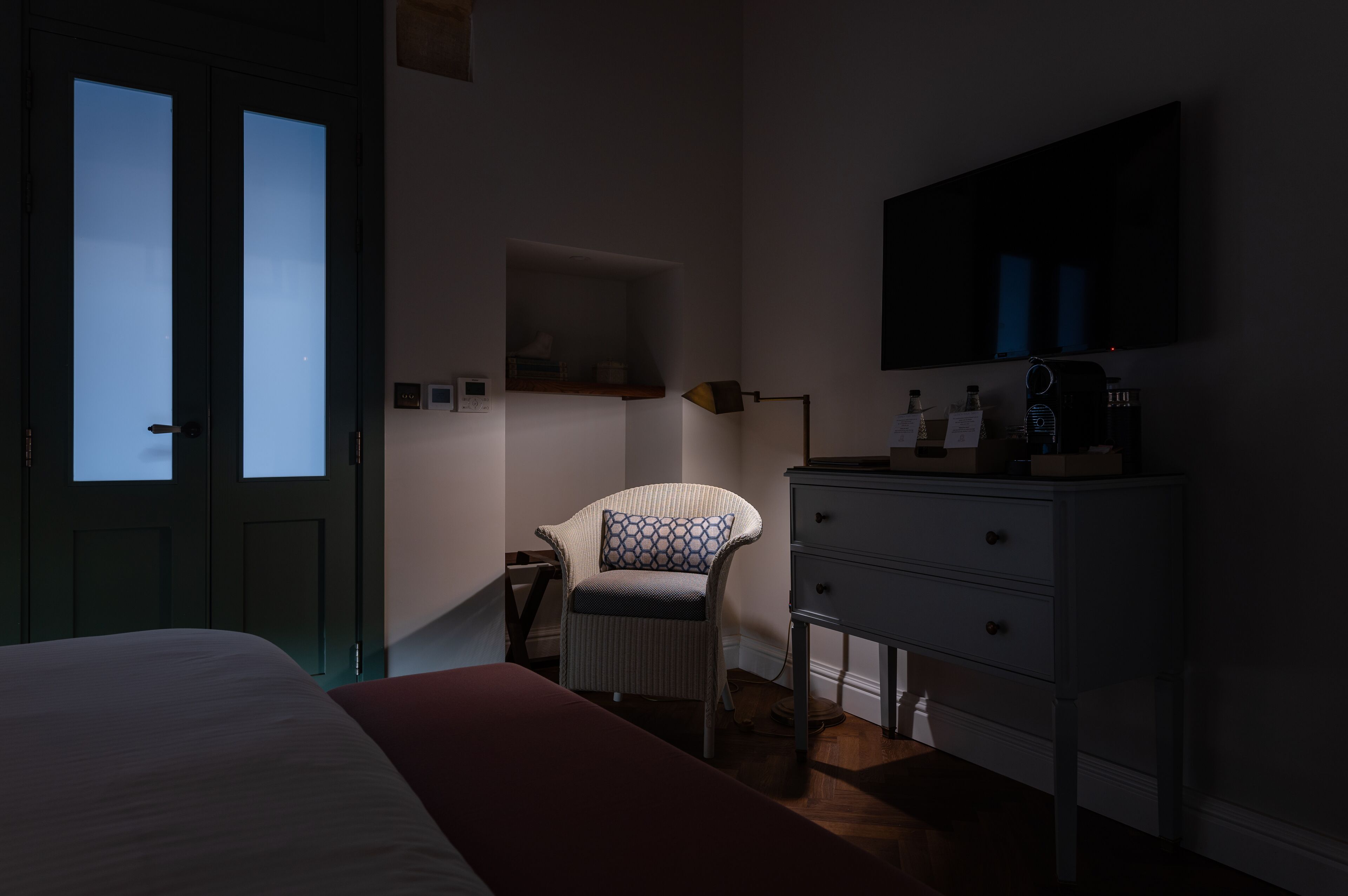 A bedroom with a bed, a chair, a dresser, and a television on the wall.