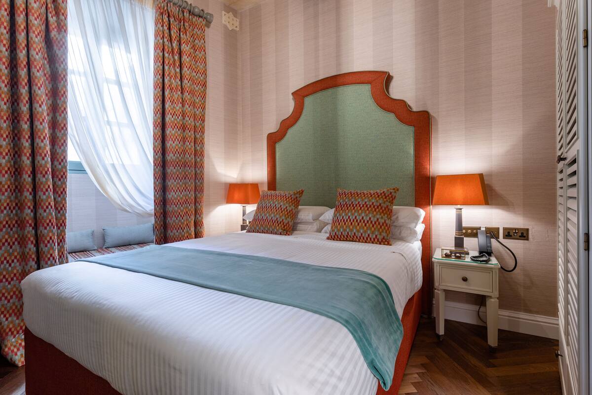 Una cama bien hecha con un cabecero estampado, dos lámparas de noche y una mesita de noche con lámpara.