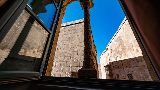 A view through a window of a building with a stone wall and an arched window frame. - Palazzo Bifora (Mdina)