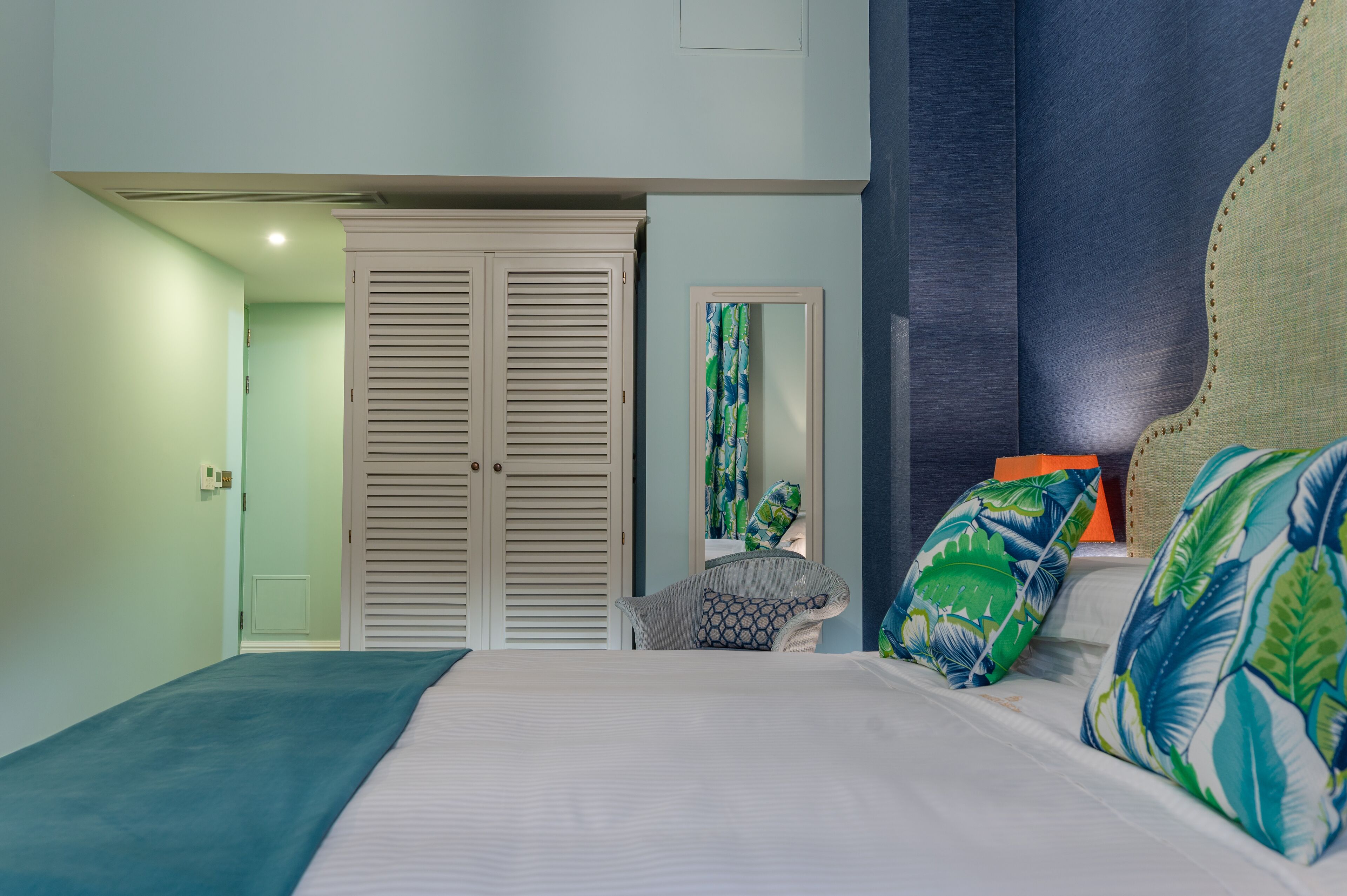 A bedroom with a bed, a chair, a wardrobe, and a mirror.