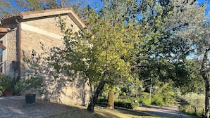 A stone building with a sloped roof, surrounded by a grassy area with trees and a paved path.