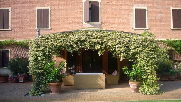 A brick building with a covered patio area featuring a sofa and a table. - Questa elegante villa offre camere perfetto per viaggi di lavoro o di coppia (Carpi)