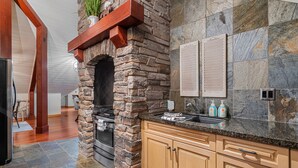 A kitchen with a stone fireplace, wooden cabinets, and a granite countertop.