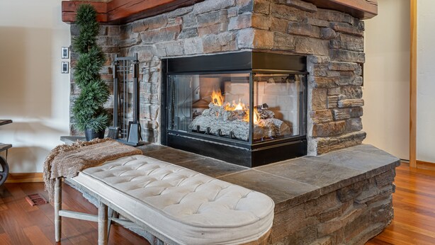 A stone fireplace with a bench in front, a potted plant to the left, and a wooden beam above.
