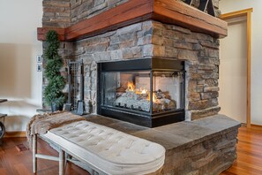 A stone fireplace with a bench in front, a potted plant to the left, and a wooden beam above. -  Penthouse~ Mountain View (Canmore)