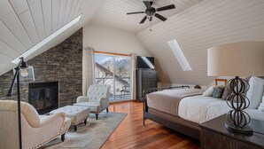 A bedroom with a stone fireplace, a bed, a TV, and a ceiling fan.