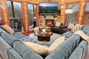 A cozy living room with a stone fireplace, a large flat-screen TV, and a comfortable seating area. - Heated In-Cabin Pool~Theatre~Game Room~Views (Sevierville)
