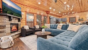 Un intérieur de chalet chaleureux avec une cheminée en pierre, un grand canapé d’angle et un coin repas.