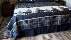 Un dormitorio con cama de madera, dos mesitas de noche, cabecero de madera, un cuadro en la pared y una alfombra estampada.