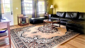 Ein Wohnzimmer mit einer schwarzen Ledersofa, einem Holztisch, einem gemusterten Teppich und einem kleinen Beistelltisch mit einer Lampe.