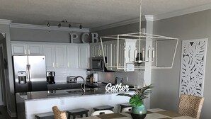 A modern kitchen with white cabinets, a central island, and a dining area with a checkered table and wicker chairs. - LUXURY 20TH FLOOR BEACHFRONT CONDO/HUGE BALCONY/BEACH SERVICE/5 STAR REVIEWS (Panama City Beach)