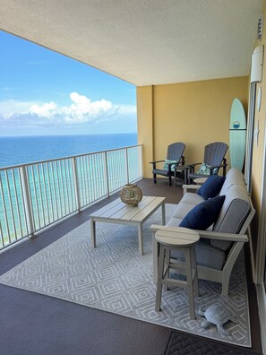 A balcony with a view of the ocean, two Adirondack chairs, a small table, and a surfboard against the wall.
